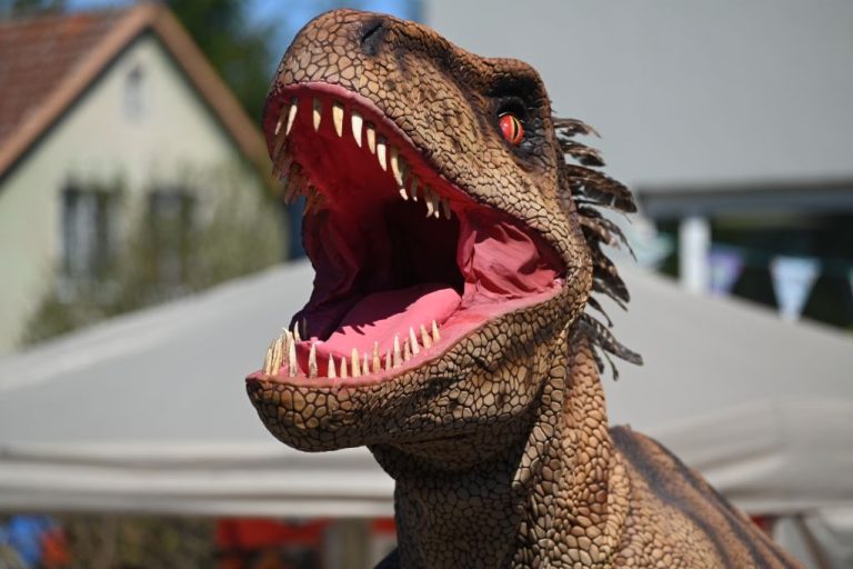 Ein großer Dinosaurier mit gestreifter Haut und leuchtend roten Augen in einem Garten.